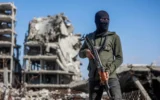 Illustration : Un terroriste du Hamas montant la garde tandis que des travailleurs égyptiens, accompagnés de membres du Comité international de la Croix-Rouge (CICR), utilisent une pelleteuse pour rechercher la dépouille du dernier otage dans le camp de réfugiés de Jabaliya, dans le nord de la bande de Gaza, le 1ᵉʳ décembre 2025. (Crédit : Omar Al-Qattaa/AFP)