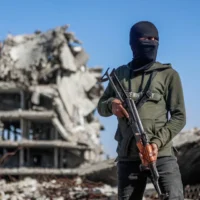 Illustration : Un terroriste du Hamas montant la garde tandis que des travailleurs égyptiens, accompagnés de membres du Comité international de la Croix-Rouge (CICR), utilisent une pelleteuse pour rechercher la dépouille du dernier otage dans le camp de réfugiés de Jabaliya, dans le nord de la bande de Gaza, le 1ᵉʳ décembre 2025. (Crédit : Omar Al-Qattaa/AFP)