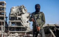 Illustration : Un terroriste du Hamas montant la garde tandis que des travailleurs égyptiens, accompagnés de membres du Comité international de la Croix-Rouge (CICR), utilisent une pelleteuse pour rechercher la dépouille du dernier otage dans le camp de réfugiés de Jabaliya, dans le nord de la bande de Gaza, le 1ᵉʳ décembre 2025. (Crédit : Omar Al-Qattaa/AFP)