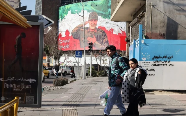 Des Iraniens passent à moto devant une immense banderole représentant l'ancien commandant de la Force Qods du Corps des gardiens de la révolution islamique (CGRI) Qasem Soleimani, à l'approche du sixième anniversaire de son assassinat en Irak, sur la place Valiasr à Téhéran, le 31 décembre 2025. (Crédit : ATTA KENARE / AFP)