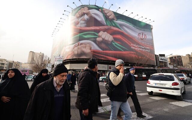 Des passants devant une grande banderole patriotique représentant le drapeau iranien, sur la place Enghelab, à Téhéran, le 14 janvier 2026. (Crédit : Atta Kenare/AFP)