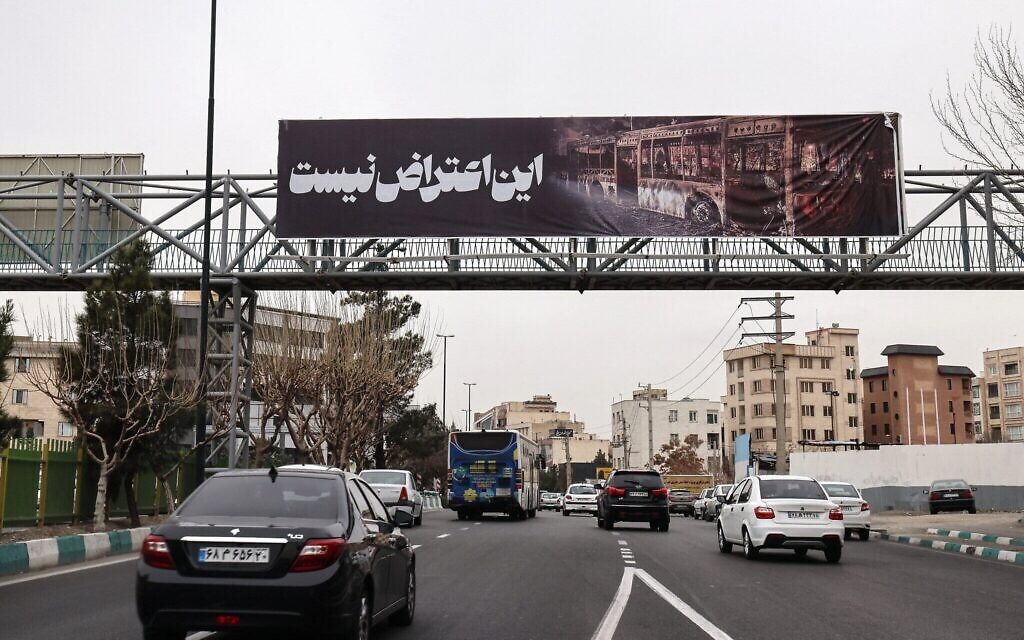 Des conducteurs se rendant à leur travail passent sous une banderole sur laquelle on peut lire "Ce n'est pas une manifestation" à côté d'une photo d'un bus incendié, à Téhéran, en Iran, le 15 janvier 2026. (Crédit : ATTA KENARE / AFP) Des conducteurs se rendant à leur travail passent sous une banderole sur laquelle on peut lire "Ce n'est pas une manifestation" à côté d'une photo d'un bus incendié, à Téhéran, en Iran, le 15 janvier 2026. (Crédit : ATTA KENARE / AFP)