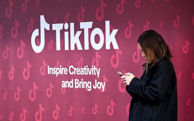 Une femme utilise son téléphone devant le stand de TikTok lors de la réunion annuelle du Forum économique mondial (WEF) à Davos, le 19 janvier 2026. (Crédit : Ina Fassbender/AFP)
