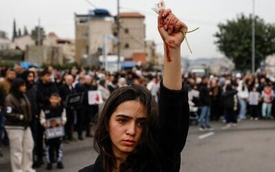 Une femme brandit des fleurs, des marques rouges visibles sur sa main, alors que des manifestants arabes se rassemblent pour protester contre ce qu’ils considèrent comme l’inaction de la police face à la recrudescence des crimes violents dans la communauté, à Sakhnin le 22 janvier 2026. (Crédit : Jalaa MAREY/AFP)