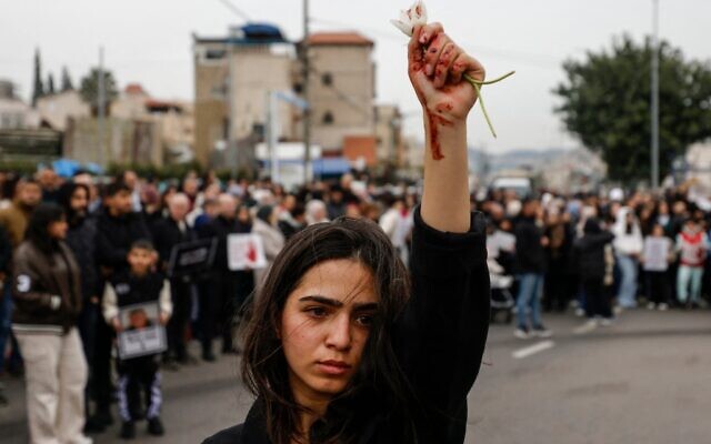 Une femme brandit des fleurs, des marques rouges visibles sur sa main, alors que des manifestants arabes se rassemblent pour protester contre ce qu’ils considèrent comme l’inaction de la police face à la recrudescence des crimes violents dans la communauté, à Sakhnin le 22 janvier 2026. (Crédit : Jalaa MAREY/AFP) Une femme brandit des fleurs, des marques rouges visibles sur sa main, alors que des manifestants arabes se rassemblent pour protester contre ce qu’ils considèrent comme l’inaction de la police face à la recrudescence des crimes violents dans la communauté, à Sakhnin le 22 janvier 2026. (Crédit : Jalaa MAREY/AFP)