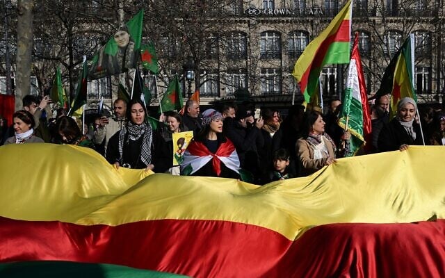 Des manifestants brandissent un immense drapeau kurde du Rojava syrien lors d'une manifestation de solidarité avec les Kurdes du nord de la Syrie, place de la République, à Paris, le 24 janvier 2026. (Crédit : Blanca Cruz / AFP)