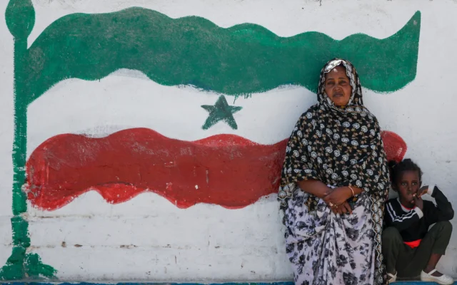 Une femme et une enfant assises devant une fresque représentant le drapeau du Somaliland, à Hargeisa, au Somaliland, une région semi-autonome séparée de la Somalie, le 9 février 2022. (Crédit : Brian Inganga/AP Photo)