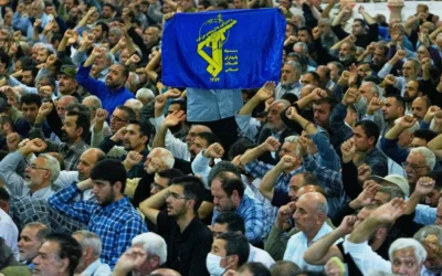 Un Iranien brandissant une banderole arborant l’emblème des Gardiens de la révolution tandis que les autres scandent des slogans lors de la cérémonie de prière du vendredi sur le campus de l’université de Téhéran, en Iran, le 13 juin 2025. (Crédit : Vahid Salemi/AP)