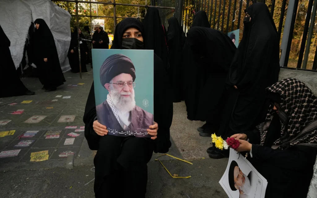 Des personnes en deuil tiennent des affiches du guide suprême iranien, l'ayatollah Ali Khamenei, au centre, et du défunt fondateur de la révolution, l'ayatollah Khomeini, lors d'une cérémonie funéraire en l'honneur de soldats inconnus tués pendant la guerre Iran-Irak de 1980-1988 et dont les dépouilles ont récemment été retrouvées sur les champs de bataille, à Téhéran, en Iran, le lundi 24 novembre 2025. (Crédit : AP Photo/Vahid Salemi) Des personnes en deuil tiennent des affiches du guide suprême iranien, l'ayatollah Ali Khamenei, au centre, et du défunt fondateur de la révolution, l'ayatollah Khomeini, lors d'une cérémonie funéraire en l'honneur de soldats inconnus tués pendant la guerre Iran-Irak de 1980-1988 et dont les dépouilles ont récemment été retrouvées sur les champs de bataille, à Téhéran, en Iran, le lundi 24 novembre 2025. (Crédit : AP Photo/Vahid Salemi)