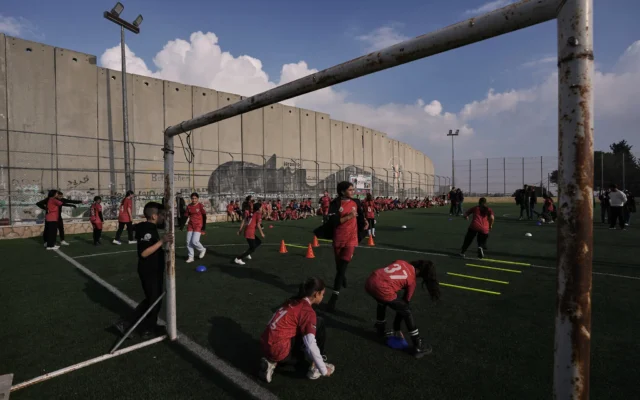 Des fillettes palestiniennes participent à un entraînement de football sur un terrain situé à côté de la barrière de sécurité israélienne dans le camp de réfugiés d'Aida, dans la ville de Bethléem, en Cisjordanie, le 26 décembre 2025. (Crédit : AP Photo/Mahmoud Illean)