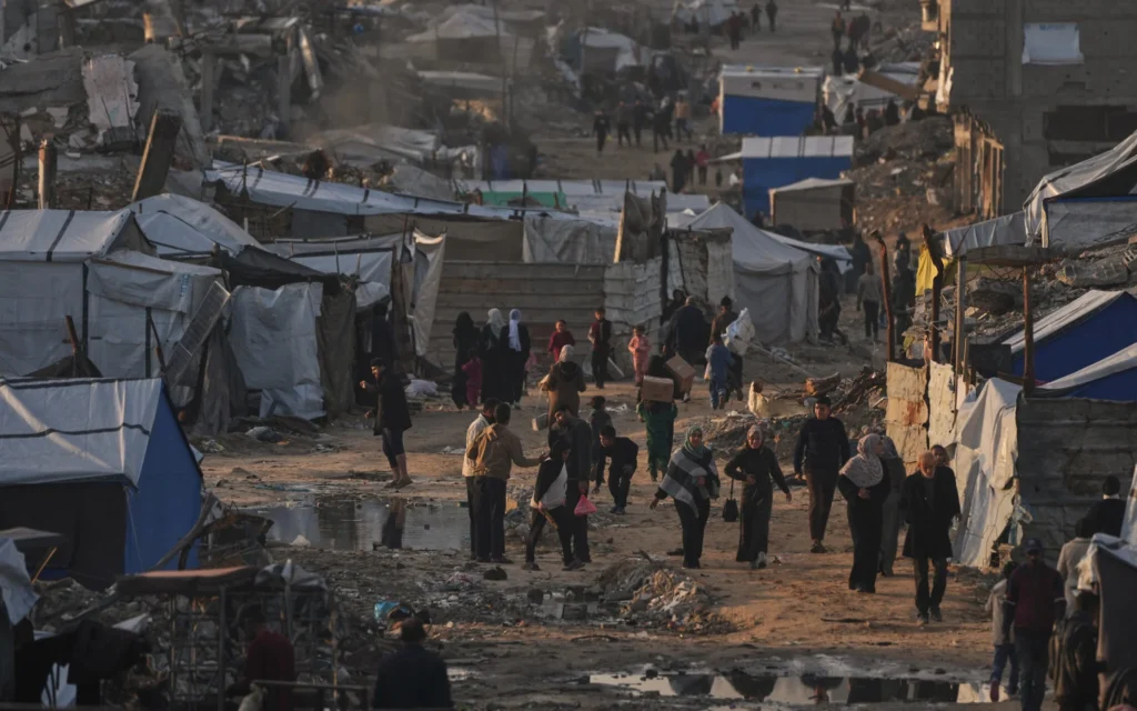 Des Palestiniens marchent dans une rue devant un campement de tentes entouré de bâtiments détruits pendant la guerre entre Israël et le Hamas à Gaza-City, le 30 décembre 2025. (Crédit : Jehad Alshrafi/AP)