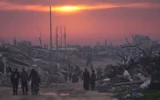 Des Palestiniens marchent parmi les ruines de bâtiments détruits alors que le soleil se couche sur Gaza-City, le 4 janvier 2026. (Crédit : AP/Jehad Alshrafi)
