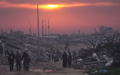 Des Palestiniens marchent parmi les ruines de bâtiments détruits alors que le soleil se couche sur Gaza-City, le 4 janvier 2026. (Crédit : AP/Jehad Alshrafi)