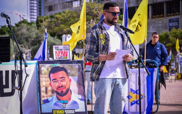 L'ancien otage Segev Kalfon s'exprimant lors d'un rassemblement vendredi après-midi en l'honneur du dernier otage à Gaza, le sergent-chef Ran Gvili, dont le portrait est exposé, sur la Place des Otages, à Tel Aviv, le 23 janvier 2026. (Crédit : Avshalom Sassoni/Flash90)