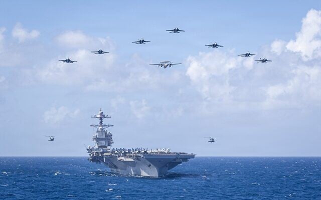 Des avions de la 8e escadre aérienne embarquée de l'US Navy volent en formation au-dessus du plus grand porte-avions au monde, le porte-avions de classe Ford USS Gerald R. Ford (CVN 78), lors de la cérémonie de passation de commandement de la 8e escadre aérienne embarquée, en mer des Caraïbes, le 19 janvier 2026. (Crédit : US Navy)