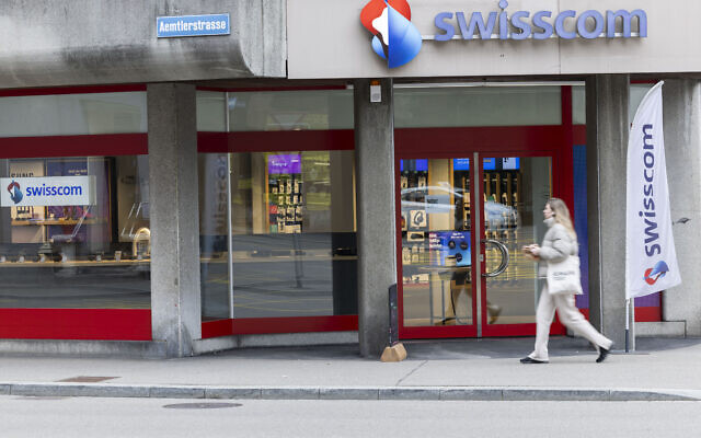 Une femme passe devant le logo de l'opérateur de télécommunications suisse Swisscom, devant une agence à Zurich, le 28 février 2024. Le géant britannique des télécommunications Vodafone a annoncé le même jour être en négociations avancées pour vendre sa filiale italienne à Swisscom, après avoir rejeté les offres du groupe Iliad du milliardaire français Xavier Noël. (Photo : Arnd Wiegmann / AFP)