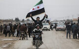 Des hommes à moto brandissent un drapeau syrien alors que les forces gouvernementales syriennes entrent dans la ville à majorité kurde de Qamishli, le 3 février 2026. (Crédit :  Bakr ALKASEM / AFP)
