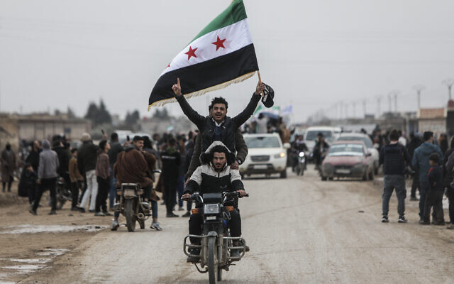 Des hommes à moto brandissent un drapeau syrien alors que les forces gouvernementales syriennes entrent dans la ville à majorité kurde de Qamishli, le 3 février 2026. (Crédit :  Bakr ALKASEM / AFP)