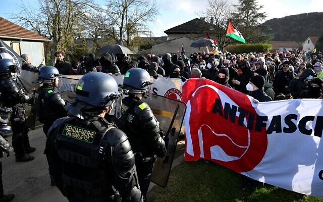 Le 7 février 2026, des membres du collectif « Fermez la !» manifestent masqués parfois ou en brandissant un drapeau palestinien sous le regard de gendarmes pour la fermeture de la « Taverne de Thor », un hangar qui accueille depuis plus de dix ans des rassemblements de MMA et des concerts néonazis à Combres-sous-les-Côtes, dans le nord-est de la France.(Crédit : Jean-Christophe Verhaegen / AFP) Le 7 février 2026, des membres du collectif « Fermez la !» manifestent masqués parfois ou en brandissant un drapeau palestinien sous le regard de gendarmes pour la fermeture de la « Taverne de Thor », un hangar qui accueille depuis plus de dix ans des rassemblements de MMA et des concerts néonazis à Combres-sous-les-Côtes, dans le nord-est de la France.(Crédit : Jean-Christophe Verhaegen / AFP)