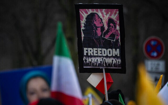 Un manifestant brandissant une pancarte sur laquelle est représentée une jeune femme brûlant la photo d'un religieux iranien, lors d'une manifestation organisée par les partisans de Maryam Radjavi, cheffe des Moudjahidine du peuple iranien (MEK), contre le gouvernement iranien, à Berlin, le 7 février 2026. (Crédit : John MacDougall/AFP)