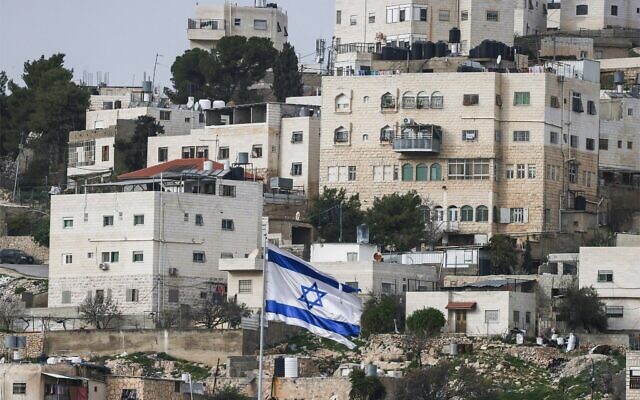 Un drapeau d'Israël flottant au-dessus de l'implantation de Beit Romano (non visible), avec des bâtiments palestiniens en arrière-plan, dans la ville de Hébron, en Cisjordanie, le 9 février 2026. (Crédit : Hazem Bader/AFP) Un drapeau d'Israël flottant au-dessus de l'implantation de Beit Romano (non visible), avec des bâtiments palestiniens en arrière-plan, dans la ville de Hébron, en Cisjordanie, le 9 février 2026. (Crédit : Hazem Bader/AFP)