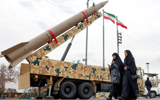 Des femmes passent devant un lanceur de missiles balistiques, lors d’un rassemblement marquant le 47ᵉ anniversaire de la révolution islamique de 1979, à Téhéran le 11 février 2026. (Crédit : AFP)