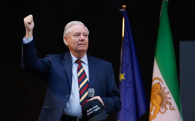 Le sénateur américain Lindsey Graham, républicain de Caroline du Sud, levant le pouce sur scène à côté d'un Européen et du drapeau national iranien historique « Lion et Soleil » lors d'une manifestation contre le régime iranien, au parc des expositions Theresienwiese, à Munich, dans le sud de l'Allemagne, en marge de la 62ᵉ Conférence sur la sécurité de Munich (MSC), le 14 février 2026. (Crédit : Michaela Stache/AFP)