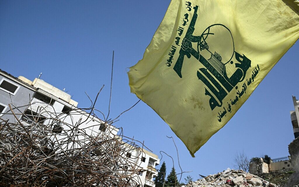 Un drapeau du groupe terroriste chiite libanais du Hezbollah flottant au-dessus des décombres d'un bâtiment touché en janvier par une frappe israélienne, dans le village de Qannarit, dans le sud du Liban, le 16 février 2026. (Crédit : Joseph Eid/AFP)