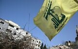 Un drapeau du groupe terroriste chiite libanais du Hezbollah flottant au-dessus des décombres d'un bâtiment touché en janvier par une frappe israélienne, dans le village de Qannarit, dans le sud du Liban, le 16 février 2026. (Crédit : Joseph Eid/AFP)
