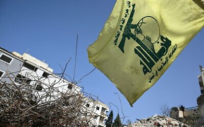 Un drapeau du groupe terroriste chiite libanais du Hezbollah flottant au-dessus des décombres d'un bâtiment touché en janvier par une frappe israélienne, dans le village de Qannarit, dans le sud du Liban, le 16 février 2026. (Crédit : Joseph Eid/AFP)