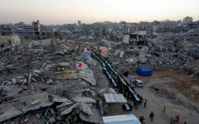 Des Gazaouis rassemblés pour un repas collectif de rupture du jeûne (iftar) organisé par la fondation turque IHH, au milieu des décombres de bâtiments détruits, à Gaza-City le 18 février 2026. (Crédit : Omar al-Qattaa/AFP)
