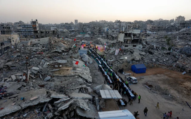 Des Gazaouis rassemblés pour un repas collectif de rupture du jeûne (iftar) organisé par la fondation turque IHH, au milieu des décombres de bâtiments détruits, à Gaza-City le 18 février 2026. (Crédit : Omar al-Qattaa/AFP) Des Gazaouis rassemblés pour un repas collectif de rupture du jeûne (iftar) organisé par la fondation turque IHH, au milieu des décombres de bâtiments détruits, à Gaza-City le 18 février 2026. (Crédit : Omar al-Qattaa/AFP)