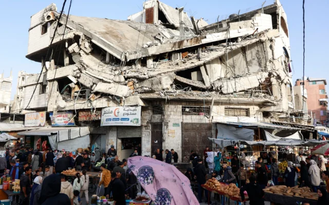 Des Palestiniens font leurs courses sous un bâtiment détruit au marché Zawiya de Gaza-City, le 18 février 2026, lors des premiers jours du mois du ramadan. (Crédit : Omar AL-QATTAA / AFP)