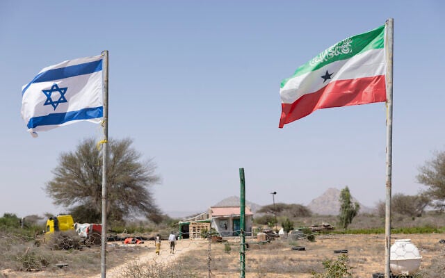 Des gens passant devant les drapeaux d'Israël et du Somaliland flottant côte à côte à l'entrée d'une exploitation fruitière, entre Hargeisa, la capitale, et la ville portuaire de Berbera, le long de l'autoroute qui relie les deux villes, alors que les musulmans célèbrent le ramadan, au Somaliland, le 19 février 2026. (Crédit : Tony Karumba/AFP)