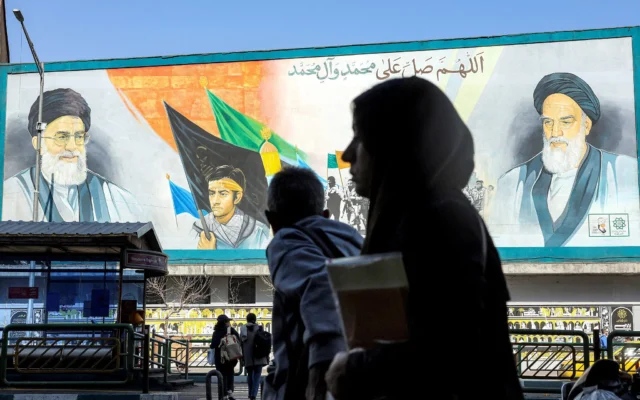 Une femme marche près d'une banderole représentant les anciens et actuels guides suprêmes de l'Iran (de droite à gauche) l'ayatollah Ruhollah Khomeini et l'ayatollah Ali Khamenei, dans une rue principale de Téhéran, le 21 février 2026. (Crédit : AFP)