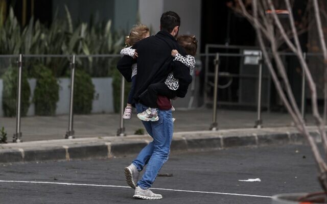 Illustration : Un homme portant deux enfants dans ses bras alors qu'il court se mettre à l'abri après le déclenchement des sirènes à Tel Aviv le 28 février 2026, à la suite de l'annonce du lancement d'une frappe préventive contre l'Iran par Israël. (Crédit : Ilia Yefimovich/AFP) Illustration : Un homme portant deux enfants dans ses bras alors qu'il court se mettre à l'abri après le déclenchement des sirènes à Tel Aviv le 28 février 2026, à la suite de l'annonce du lancement d'une frappe préventive contre l'Iran par Israël. (Crédit : Ilia Yefimovich/AFP)