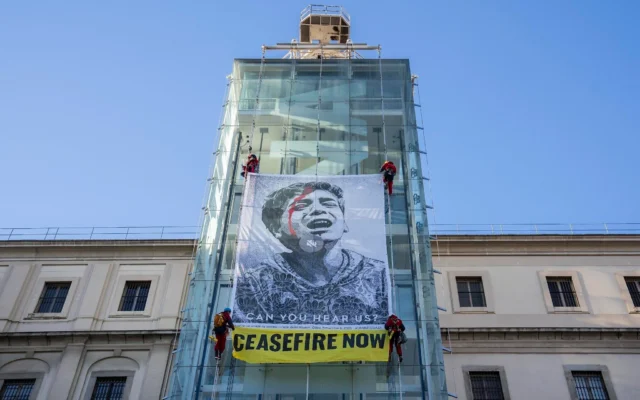 Des activistes de Greenpeace accrochent une illustration de l’artiste américain Shepard Fairey intitulée « Obey » à l’extérieur du musée Reina Sofia, avec une image prise par le photojournaliste gazaoui Belal Khaled, qui montre un enfant palestinien appelant à l’aide, Madrid, Espagne, 24 janvier 2024. (Crédit : Bernat Armangue/AP) Des activistes de Greenpeace accrochent une illustration de l’artiste américain Shepard Fairey intitulée « Obey » à l’extérieur du musée Reina Sofia, avec une image prise par le photojournaliste gazaoui Belal Khaled, qui montre un enfant palestinien appelant à l’aide, Madrid, Espagne, 24 janvier 2024. (Crédit : Bernat Armangue/AP)