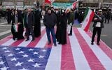 Des personnes se tenant sur une bannière représentant le drapeau américain alors qu'elles assistent à un rassemblement annuel marquant la Révolution islamique de 1979 dans la rue Azadi (Liberté), à Téhéran, en Iran, le 11 février 2026. (Crédit : Vahid Salemi/AP)