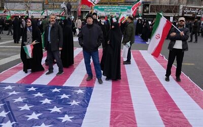 Des personnes se tenant sur une bannière représentant le drapeau américain alors qu'elles assistent à un rassemblement annuel marquant la Révolution islamique de 1979 dans la rue Azadi (Liberté), à Téhéran, en Iran, le 11 février 2026. (Crédit : Vahid Salemi/AP) Des personnes se tenant sur une bannière représentant le drapeau américain alors qu'elles assistent à un rassemblement annuel marquant la Révolution islamique de 1979 dans la rue Azadi (Liberté), à Téhéran, en Iran, le 11 février 2026. (Crédit : Vahid Salemi/AP)