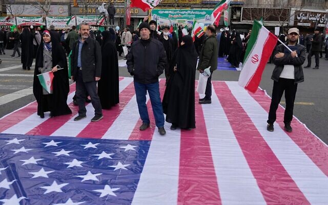 Des personnes se tenant sur une bannière représentant le drapeau américain alors qu'elles assistent à un rassemblement annuel marquant la Révolution islamique de 1979 dans la rue Azadi (Liberté), à Téhéran, en Iran, le 11 février 2026. (Crédit : Vahid Salemi/AP) Des personnes se tenant sur une bannière représentant le drapeau américain alors qu'elles assistent à un rassemblement annuel marquant la Révolution islamique de 1979 dans la rue Azadi (Liberté), à Téhéran, en Iran, le 11 février 2026. (Crédit : Vahid Salemi/AP)
