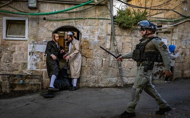 Un agent de la police des frontières passant devant des Juifs haredim, dans le quartier de Mea Shearim, à Jérusalem, le 15 avril 2025. (Crédit : Chaïm Goldberg/Flash90)