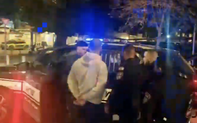 L'activiste radicale Ziv Barnes, vêtu d'un haut blanc, arrêté par la police après avoir manifesté devant l'appartement de Lucy Aharish, présentatrice arabe israélienne de la Treizième chaîne, le 23 février 2026. (Crédit : Capture d'écran vidéo/X)