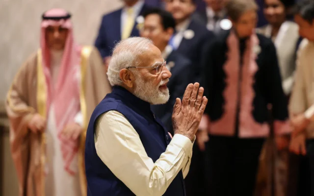 Le Premier ministre indien Narendra Modi fait un geste alors qu’il se joint aux dirigeants et représentants mondiaux pour une photo de groupe lors du Sommet sur l’impact de l’IA à New Delhi, le 19 février 2026. (Crédit : Ludovic MARIN / AFP)