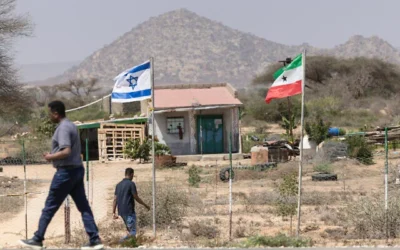 Des personnes passent devant les drapeaux d'Israël et du Somaliland, à l'entrée d'une ferme fruitière située entre la capitale, Hargeisa, et la ville portuaire de Berbera, en plein mois du Ramadan, au Somaliland, le 19 février 2026. (Tony KARUMBA / AFP)