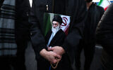Un homme tenant une affiche du guide suprême iranien, l'ayatollah Ali Khamenei, éliminé lors d'une frappe conjointe des États-Unis et d'Israël, alors qu'il se joint à d'autres personnes en deuil sur une place de Téhéran, le 1ᵉʳ mars 2026. L'ayatollah Ali Khamenei, guide suprême de l'Iran depuis 1989 et ennemi juré de l'Occident, a été tué lors de la première salve d'une attaque massive menée par les États-Unis et Israël qui s'est prolongée jusqu'au 1er mars, alors que les deux puissances cherchent à renverser la République islamique. (Crédit : Atta Kenare/AFP)