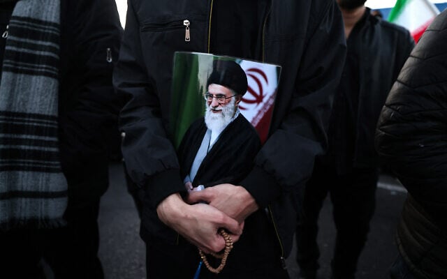 Un homme tenant une affiche du guide suprême iranien, l'ayatollah Ali Khamenei, éliminé lors d'une frappe conjointe des États-Unis et d'Israël, alors qu'il se joint à d'autres personnes en deuil sur une place de Téhéran, le 1ᵉʳ mars 2026. L'ayatollah Ali Khamenei, guide suprême de l'Iran depuis 1989 et ennemi juré de l'Occident, a été tué lors de la première salve d'une attaque massive menée par les États-Unis et Israël qui s'est prolongée jusqu'au 1er mars, alors que les deux puissances cherchent à renverser la République islamique. (Crédit : Atta Kenare/AFP)