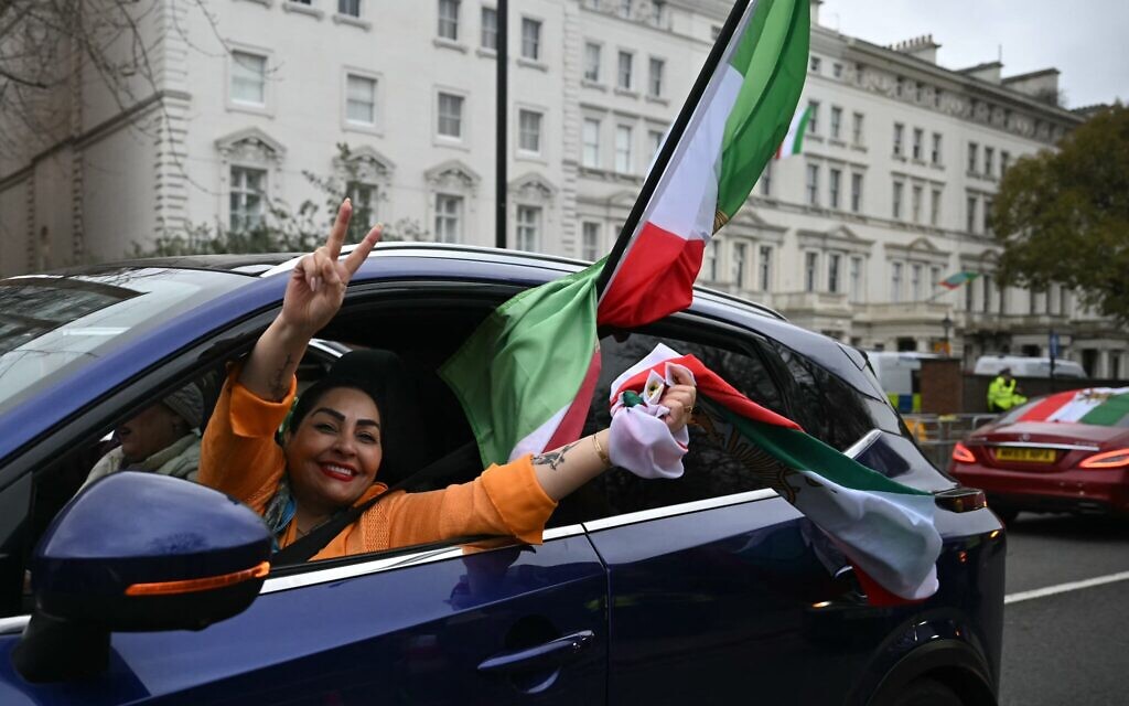 Une femme agitant un drapeau iranien d'avant la Révolution de 1979, orné de l'emblème du lion et du soleil, depuis la fenêtre d'une voiture lors d'une célébration, devant l'ambassade d'Iran, dans le centre-ville de Londres, le 1ᵉʳ mars 2026. (Crédit : Justin Tallis/AFP)