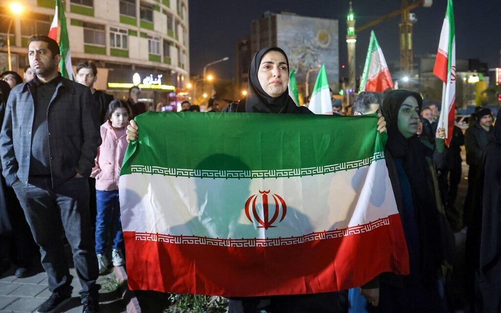 Une femme en deuil se tient debout avec un drapeau national iranien lors d'une veillée commémorative, au lendemain de l'assassinat du guide suprême iranien Ali Khamenei, tué lors d'une frappe conjointe des États-Unis et d'Israël, à Téhéran, en Iran, le 1er mars 2026. (Crédit : AFP)
