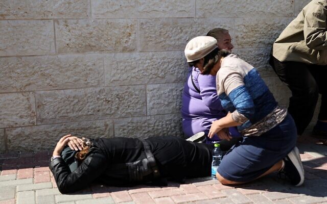 Des personnes tentant de se protéger alors que les sirènes retentissent pendant les funérailles de Sarah et Ronit Elimelech, au lendemain d'une frappe de missile sur Bet Shemesh qui a fait plusieurs morts, le 2 mars 2026. (Crédit : Ilia Yefimovich/AFP)