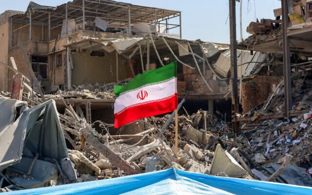Un drapeau iranien au milieu des décombres et des débris à côté d'un immeuble résidentiel détruit, non loin de la place Ferdowsi, à Téhéran, le 3 mars 2026. (Crédit : Atta Kenare/AFP)